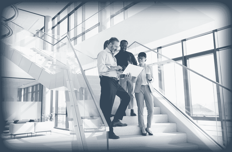 Quatre collègues discutent sur un escalier moderne dans un bureau lumineux avec de grandes fenêtres.