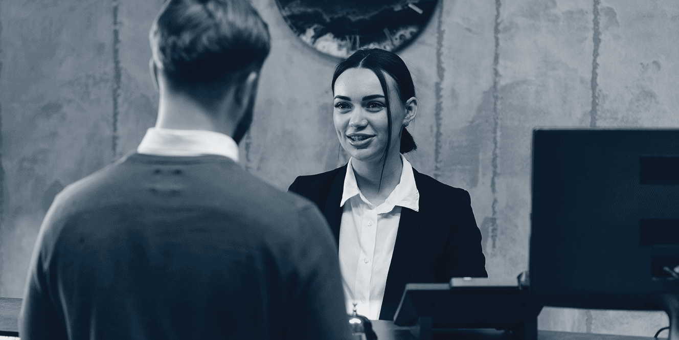 Une femme souriante en veste parle avec un homme vu de dos dans un bureau moderne.