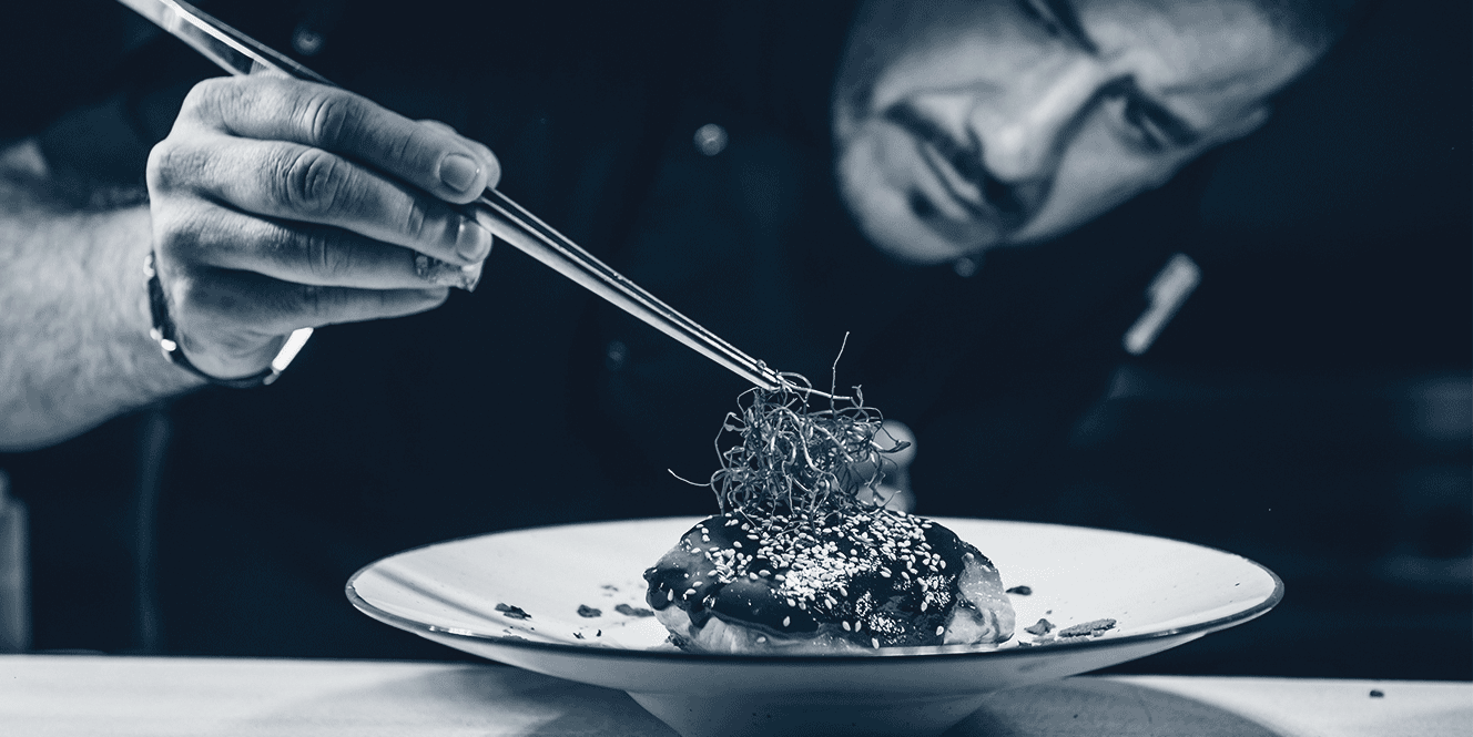 Un chef utilise des pinces pour placer des garnitures délicates sur un plat sophistiqué.
