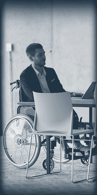 Homme en fauteuil roulant travaillant sur un ordinateur portable à une table dans un bureau.