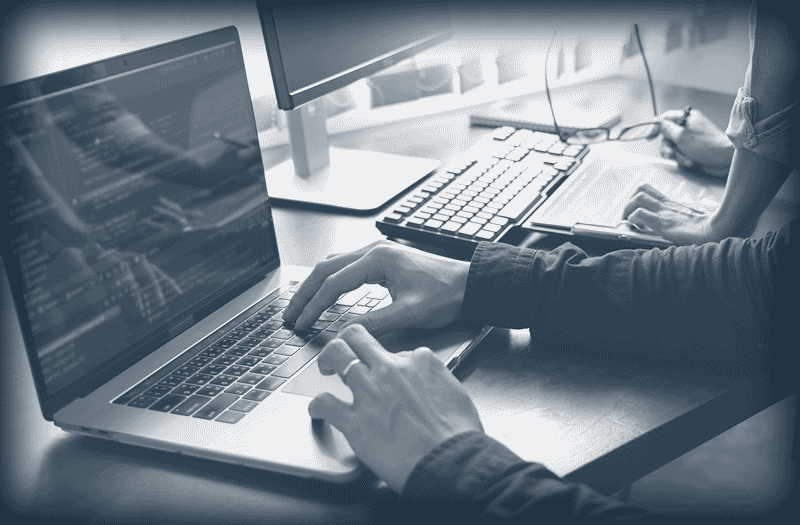 Deux personnes travaillant côte à côte sur un ordinateur portable et une tablette avec un clavier et écran.