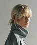 Profile of a blonde woman with a ponytail wearing a gray turtleneck sweater.