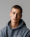 Young man with short hair wearing a blue hoodie against a plain gray background.