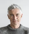 Portrait of a middle-aged man with gray hair wearing a gray sweater against a white background.