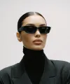 Woman in black blazer, turtleneck, and sunglasses with hair pulled back, against a plain light background.