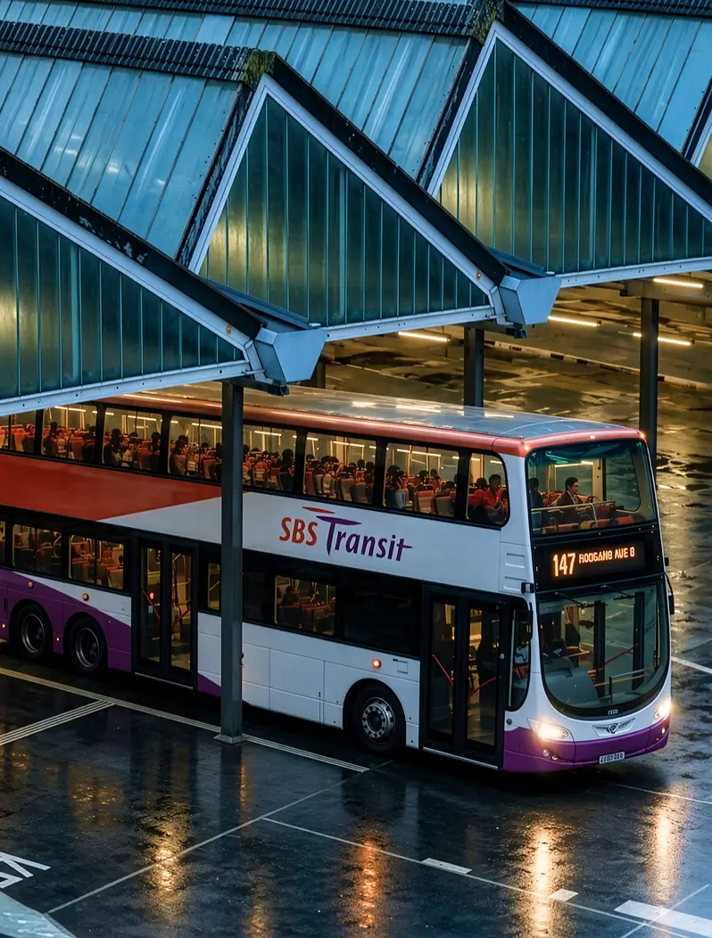 Double-decker SBS Transit bus parked under a shelter at a bus terminal on a wet pavement, with passengers seated inside and route number 147 displayed on the front.