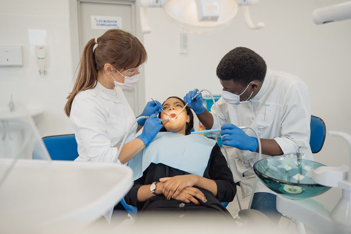 Dentists wearing masks and gloves performing dental treatment on a female patient in a clinic.
