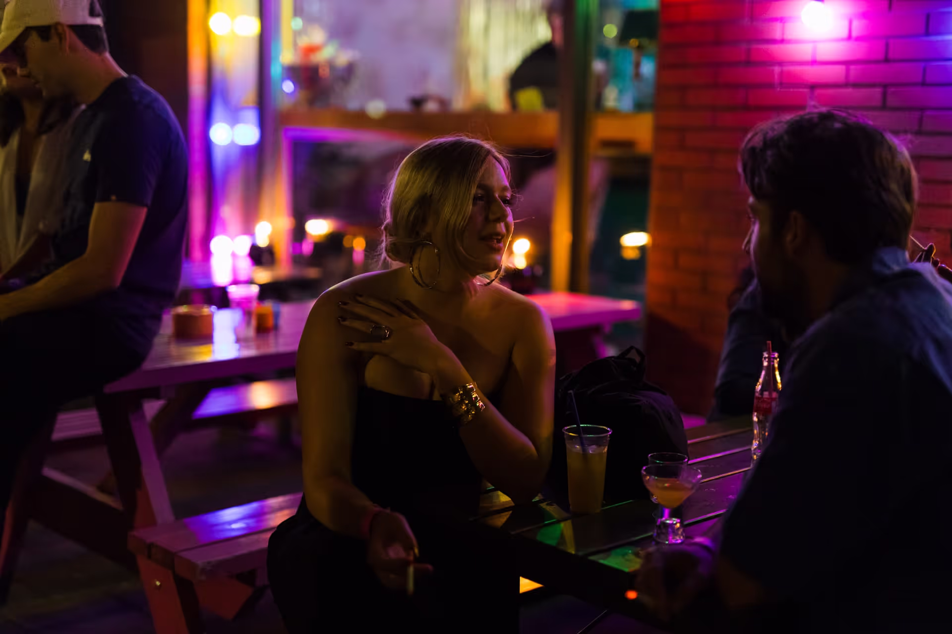 Vrouw in zwarte jurk rookt een sigaret buiten bij een trendy bar in Amsterdam.