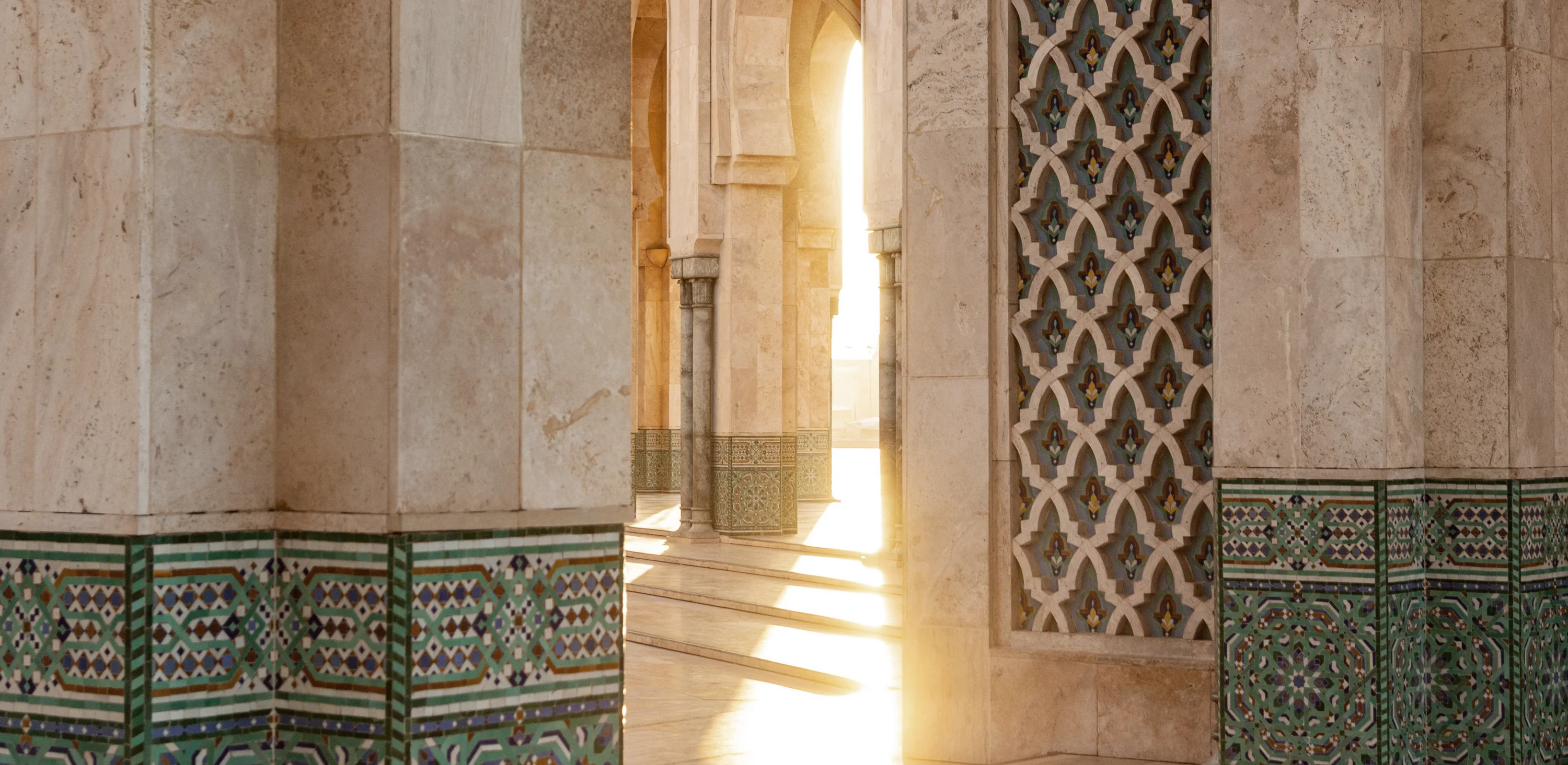 Late sun falling through a mosque archway, across patterned stone and zellij tilework.