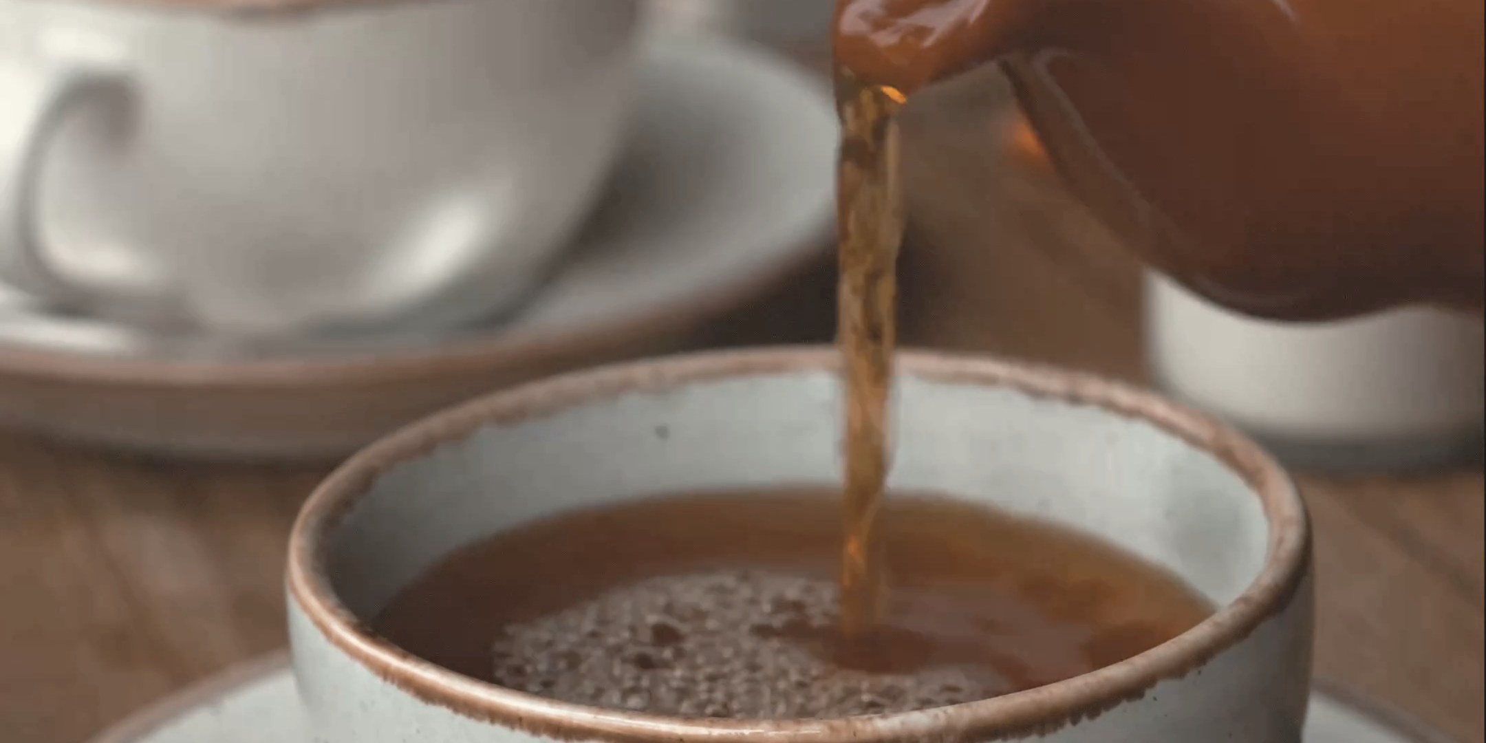 Chai poured in a thin stream from a pot into a stoneware cup.