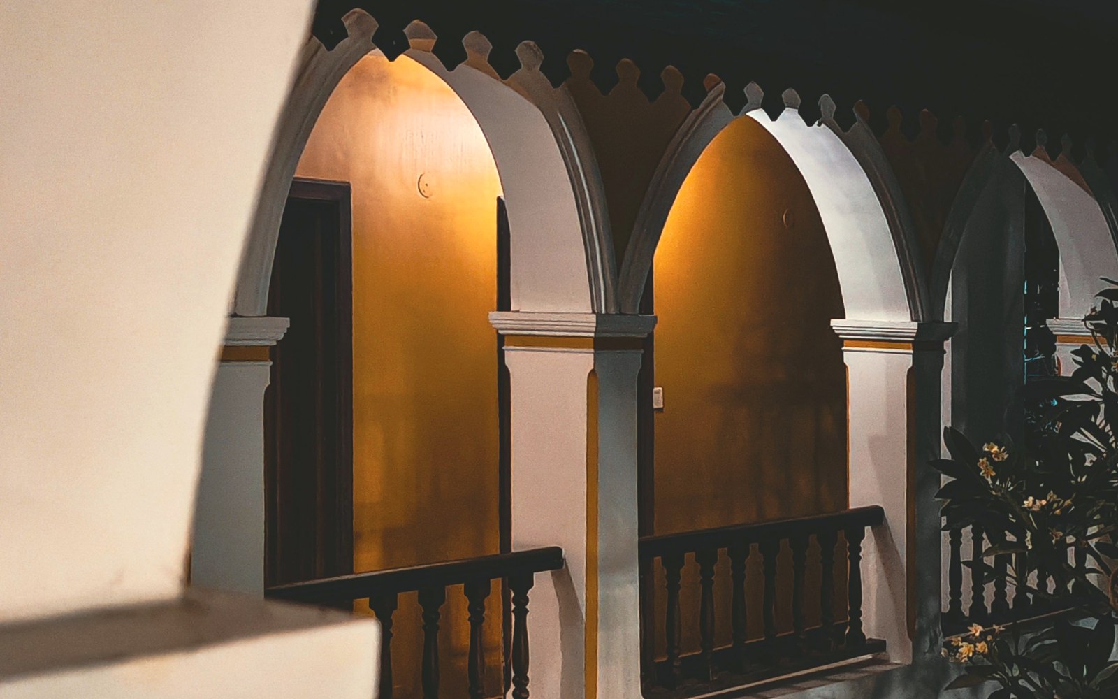 Lamplit arches of a verandah at night — warm light held inside the dark