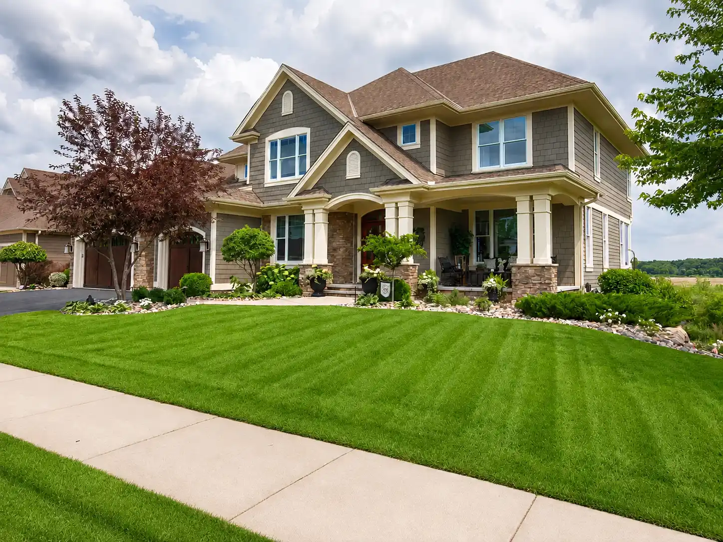 Large two-story house with brown roof, gray siding, landscaped front yard, and green lawn.