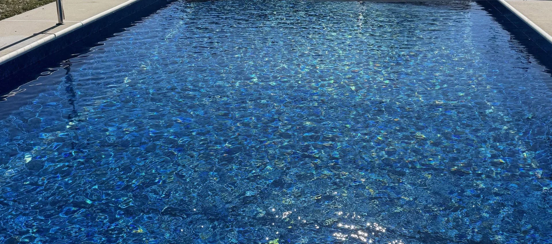 Clear water in a blue swimming pool with sunlight reflecting on its rippling surface.