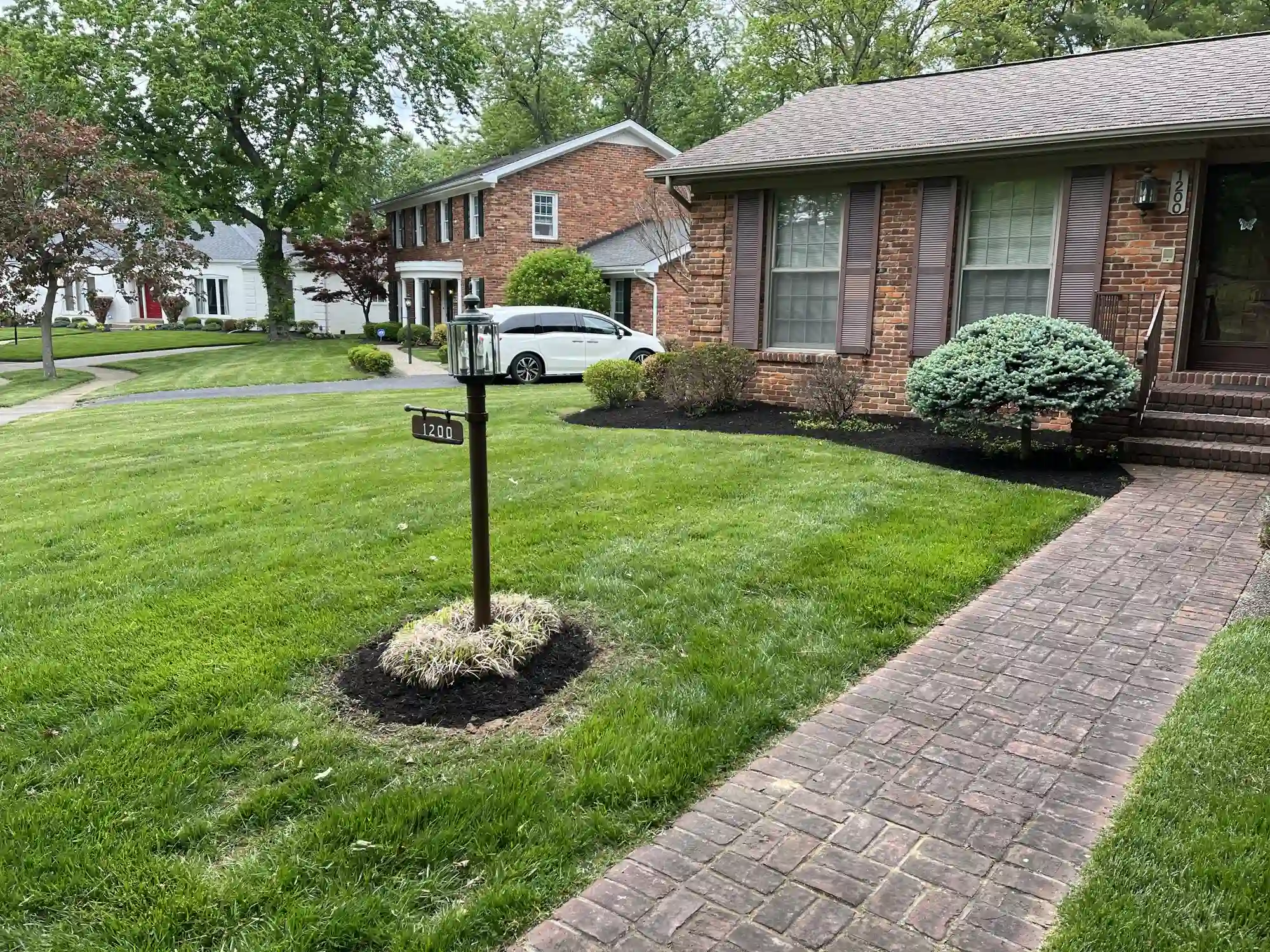 Brick house with brown shutters, manicured lawn, mailbox with 1200, and a brick walkway.