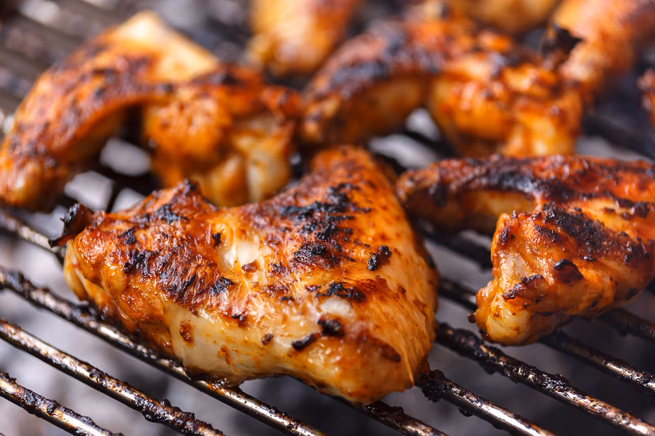 Grilled chicken wings cooking on a barbecue grill with char marks and a golden brown color.