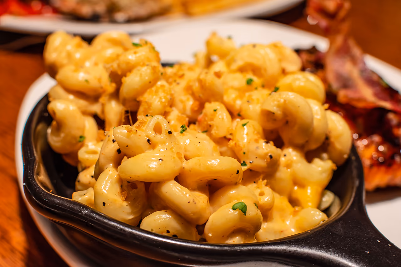 Close-up of creamy mac and cheese in a black dish garnished with pepper and herbs.