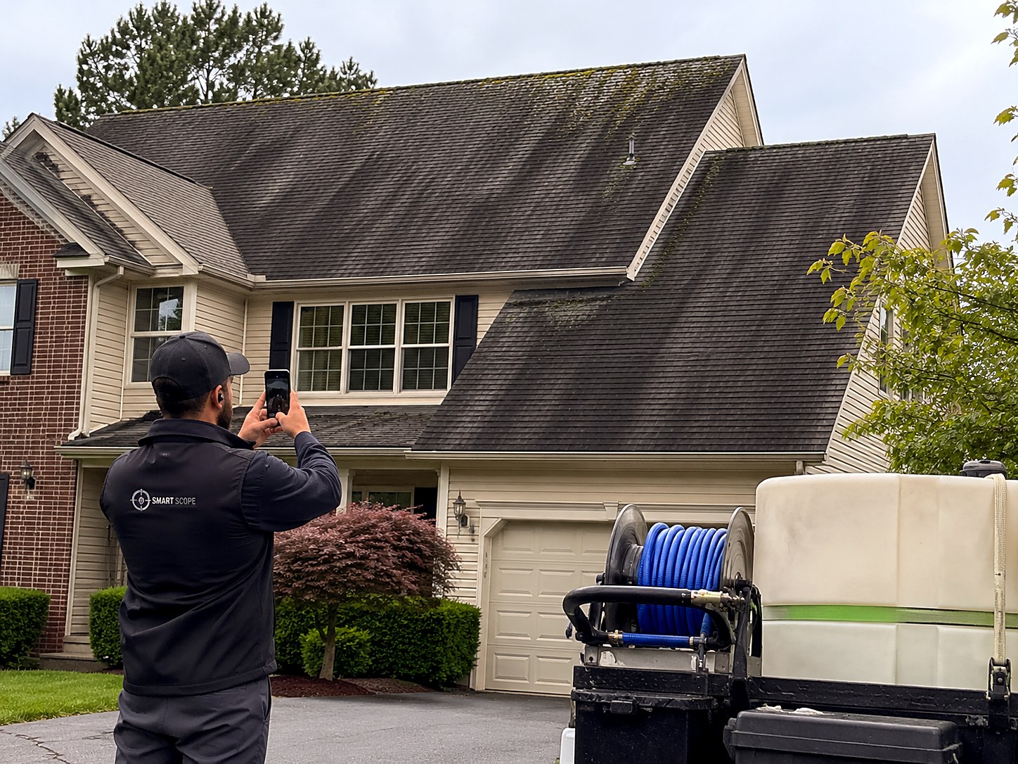 Smart Scope tech photographing heavy black streaking and ridge moss on architectural shingles before a roof soft wash, rig staged in the driveway