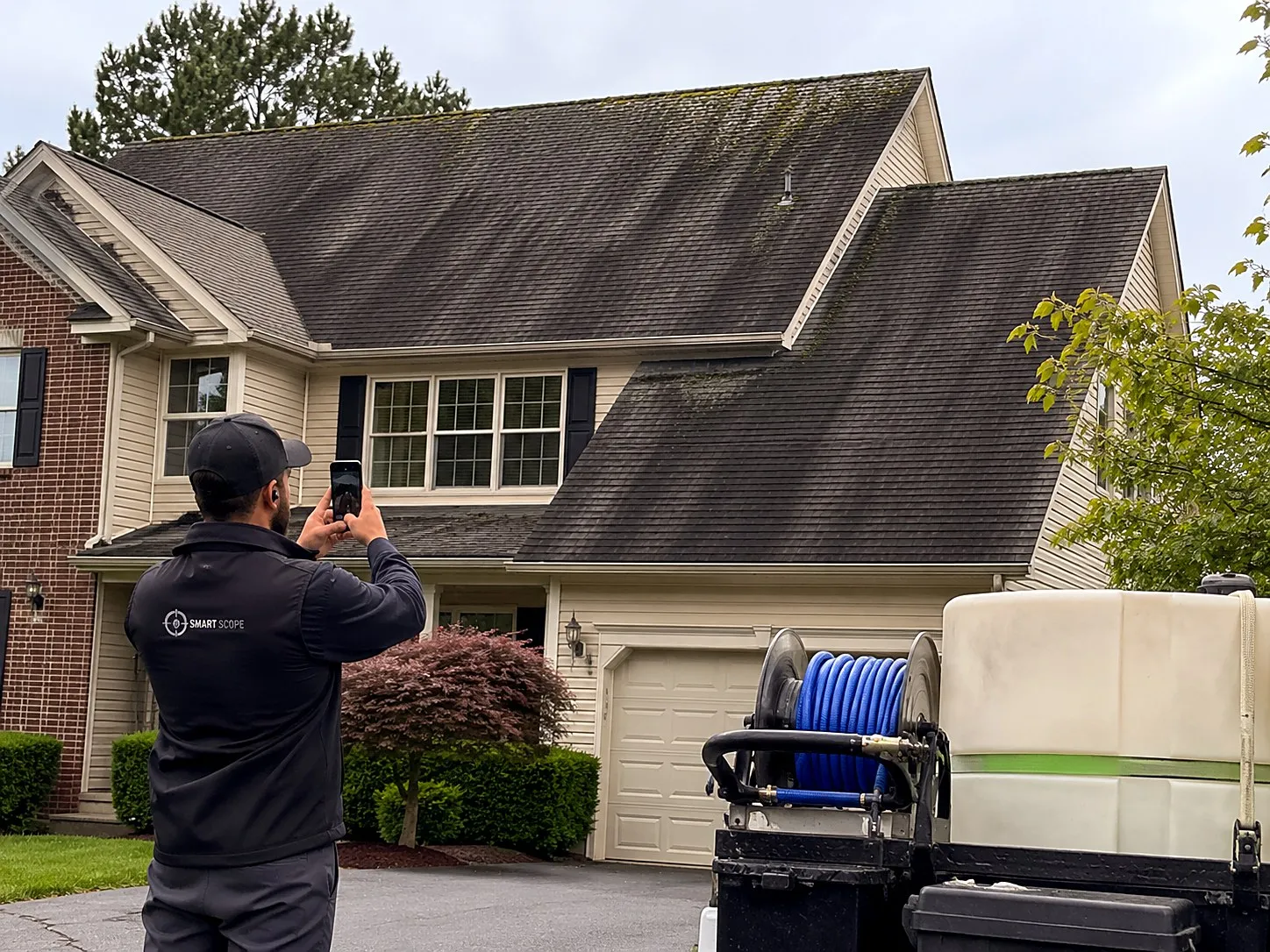 Smart Scope tech photographing heavy black streaking and ridge moss on architectural shingles before a roof soft wash, rig staged in the driveway