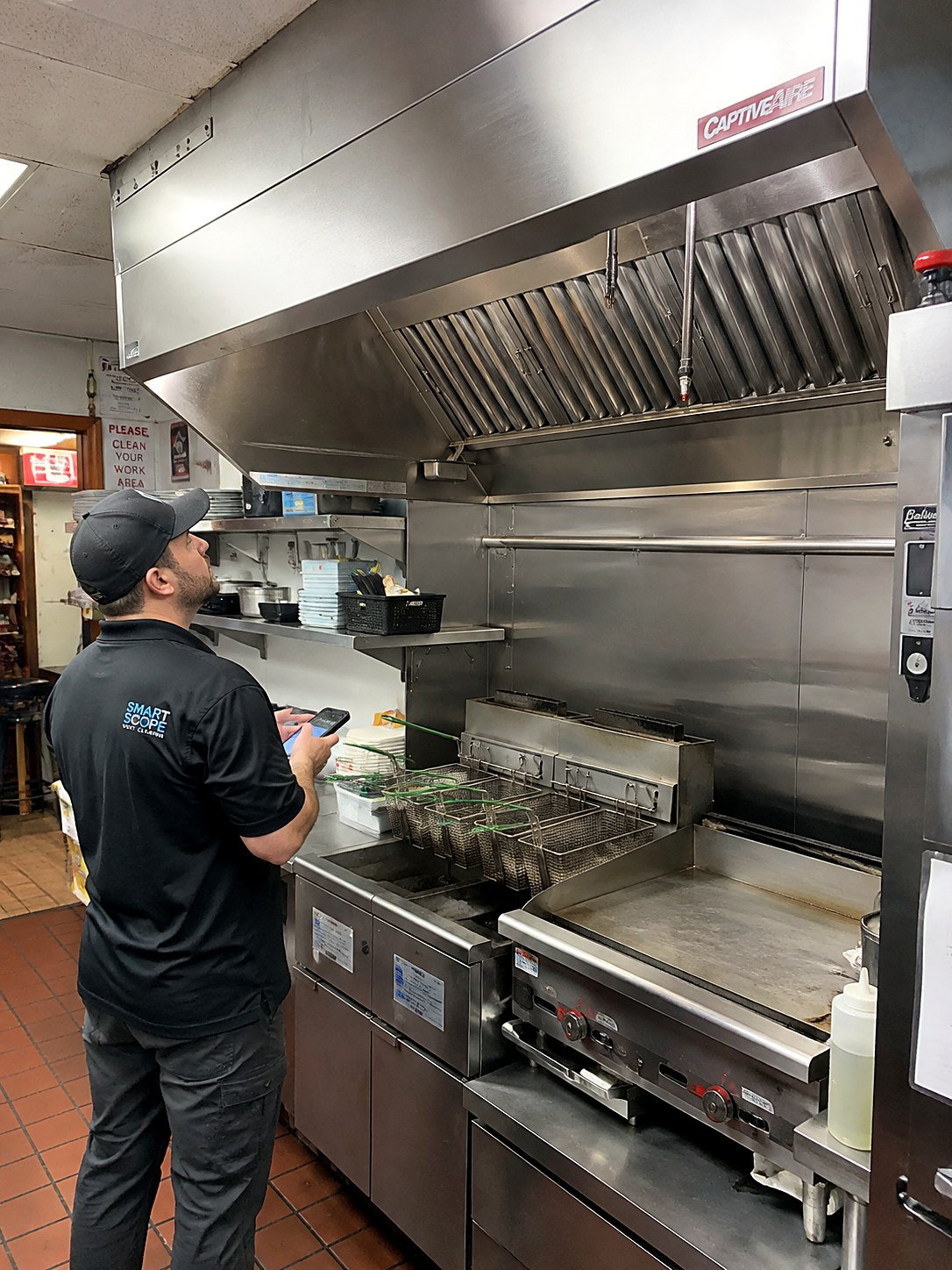 Hood cleaning tech photographing a single ten-foot hood over the fryers and flat-top in a small diner kitchen