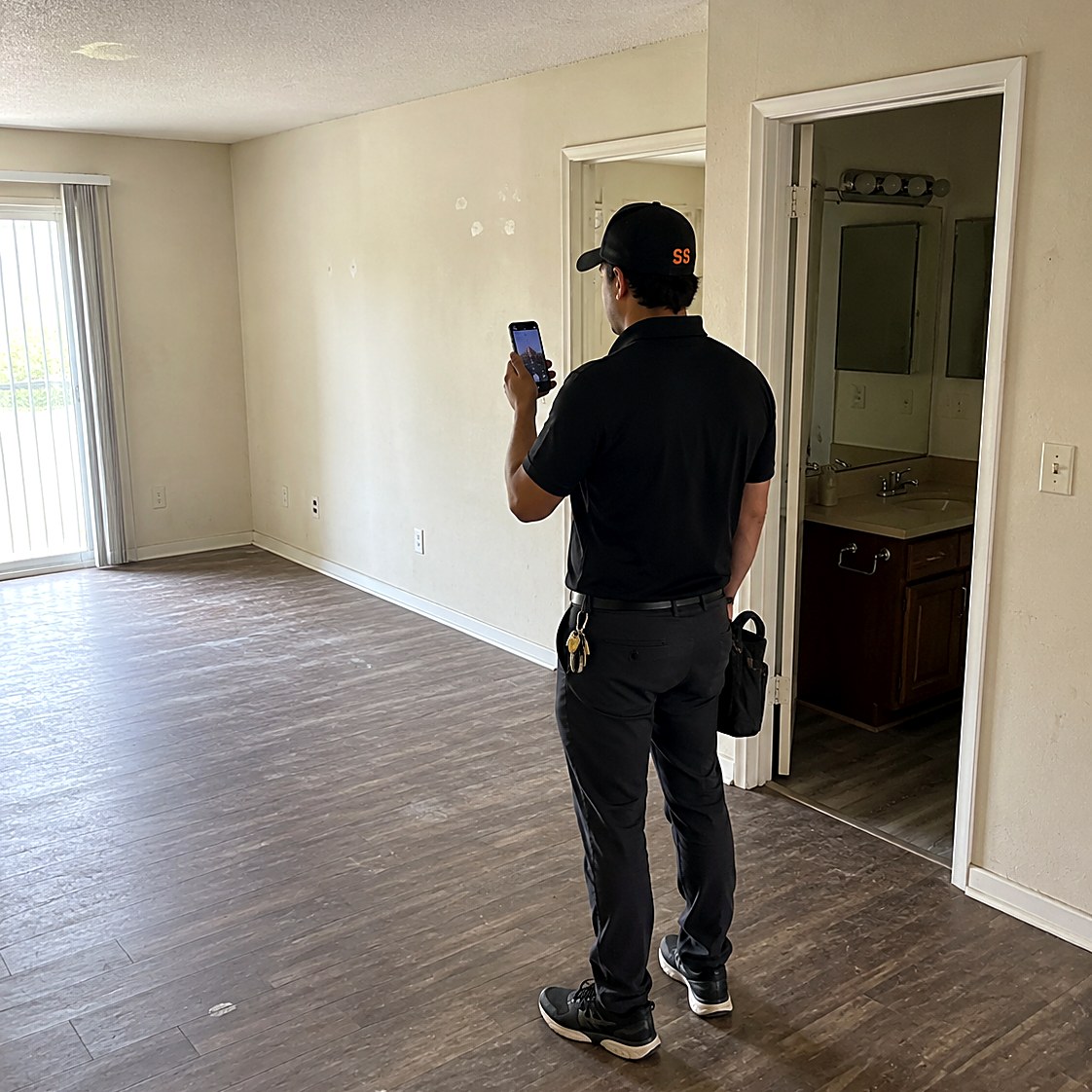 Technician photographing patched drywall in an empty apartment living room during a unit turn walkthrough