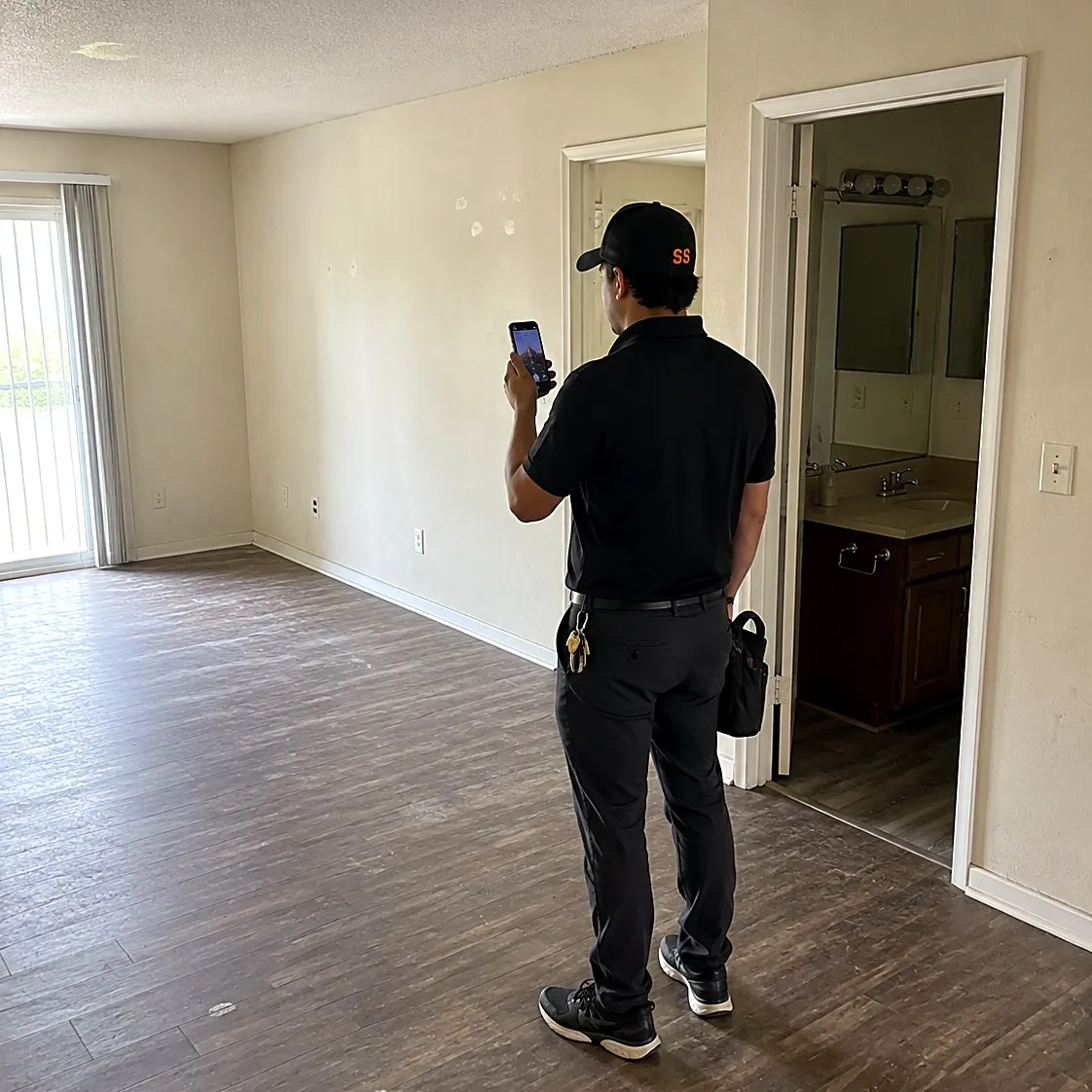 Technician photographing patched drywall in an empty apartment living room during a unit turn walkthrough