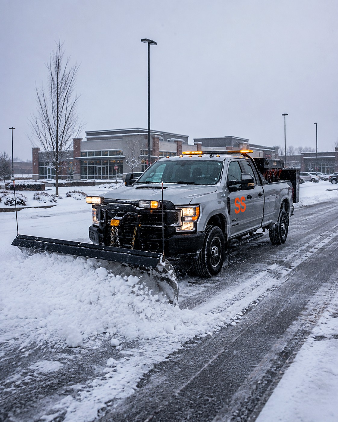 Snow plowing crew's plow truck clearing a snowy commercial parking lot