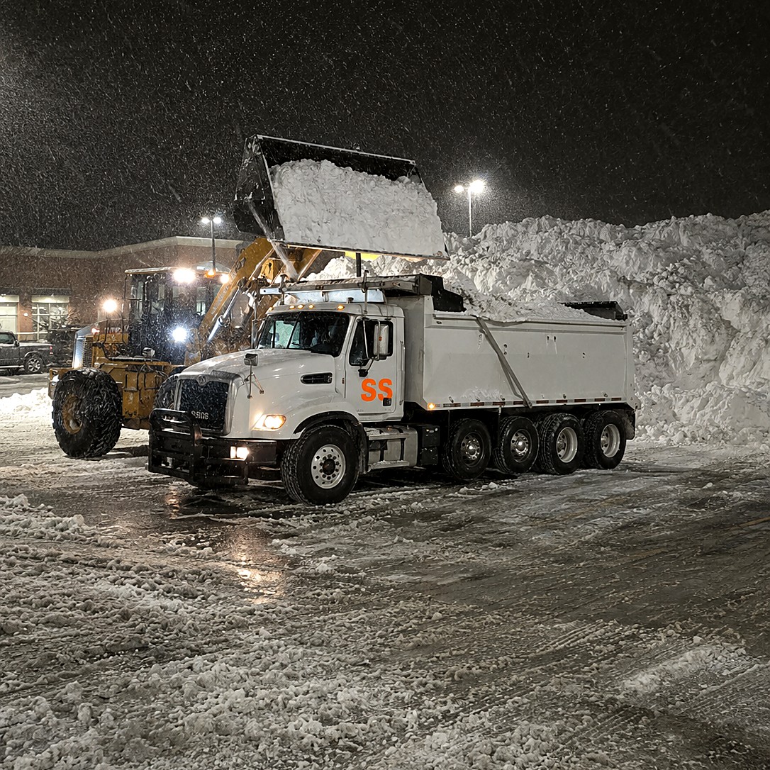 Loader filling a dump truck with snow overnight during an emergency haul-off after a blizzard