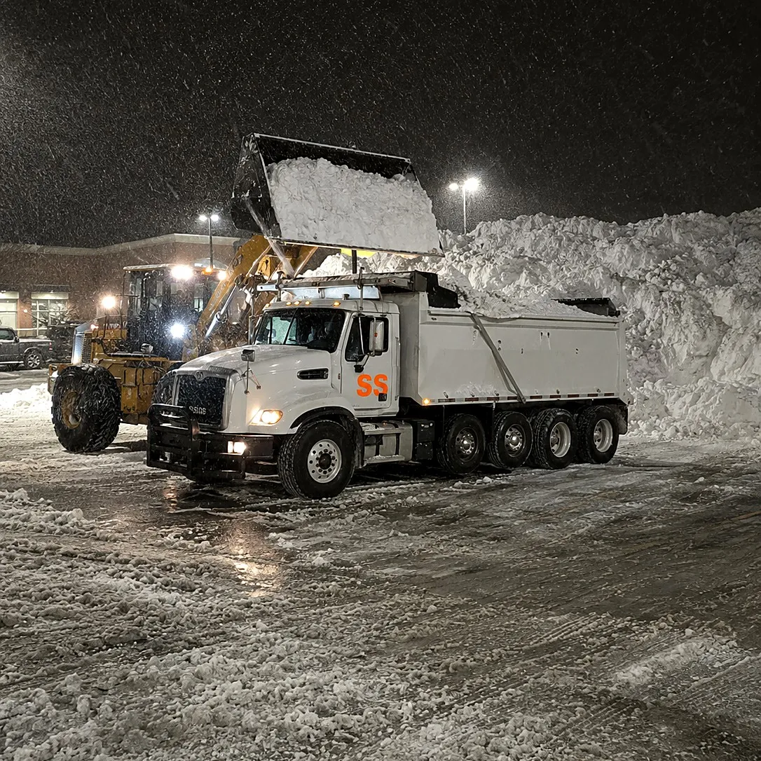 Loader filling a dump truck with snow overnight during an emergency haul-off after a blizzard