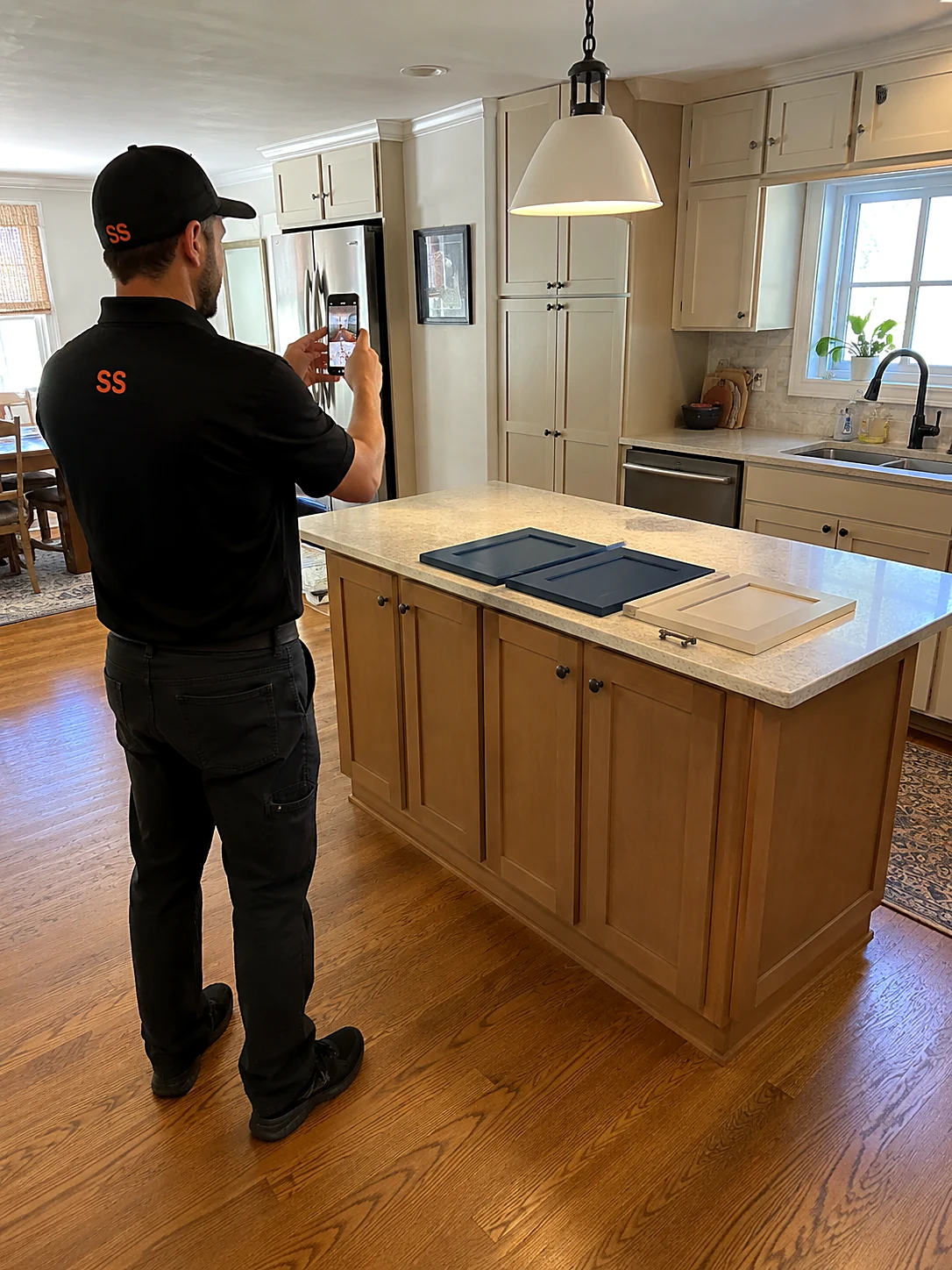 Refacer photographing a kitchen island with navy accent sample door fronts laid on the countertop, pantry cabinets in the background