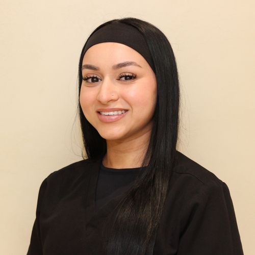 Femme souriante aux cheveux courts et bouclés portant une chemise blanche sur fond jaune.
