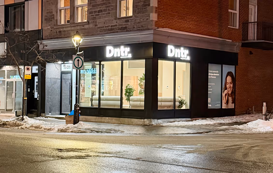 Façade éclairée d'une clinique dentaire nommée Dntr. à un coin de rue enneigé la nuit.