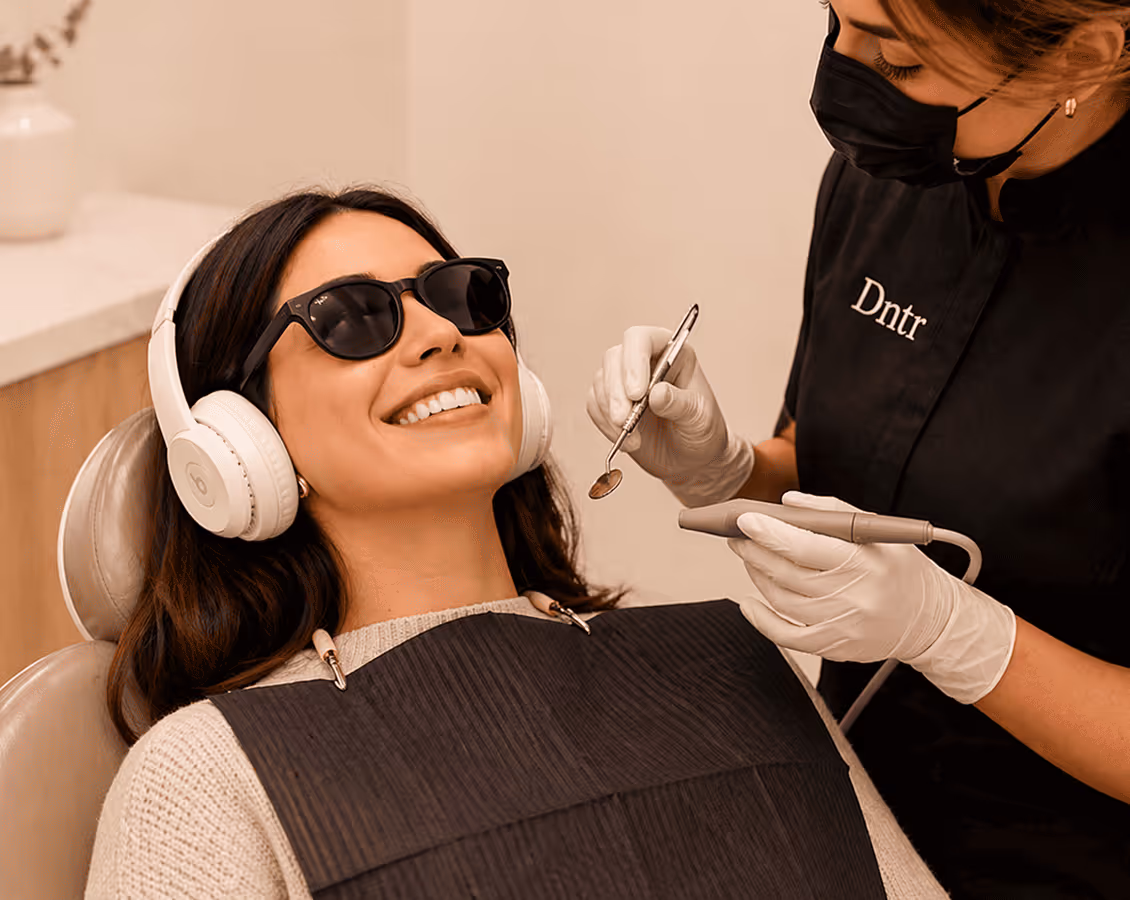 Une patiente souriante avec casque et lunettes, examinée par une dentiste portant un masque noir.
