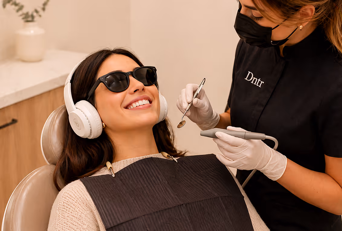 Femme souriante avec lunettes de soleil et casque à un rendez-vous dentaire, dentiste portant un masque noir.