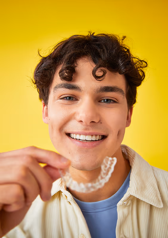 Jeune homme souriant tenant un aligneur invisible transparent près de son visage.