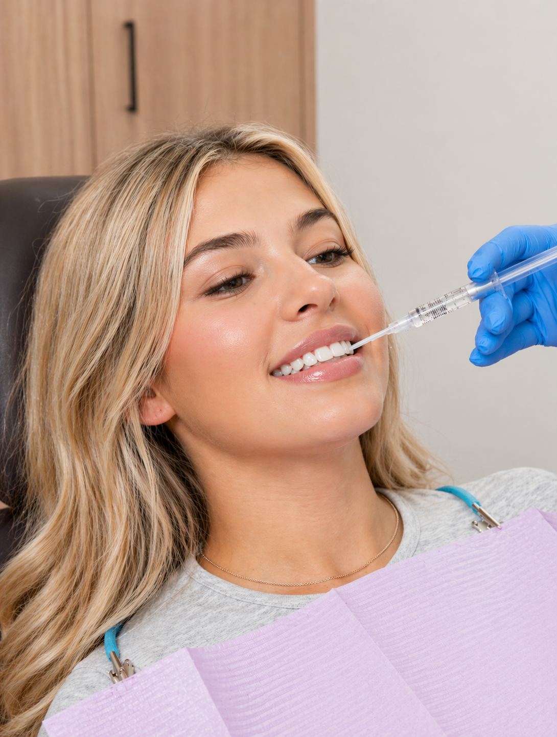 Une femme souriante compare la teinte de ses dents à un échantillon de nuances pour facettes dentaires.