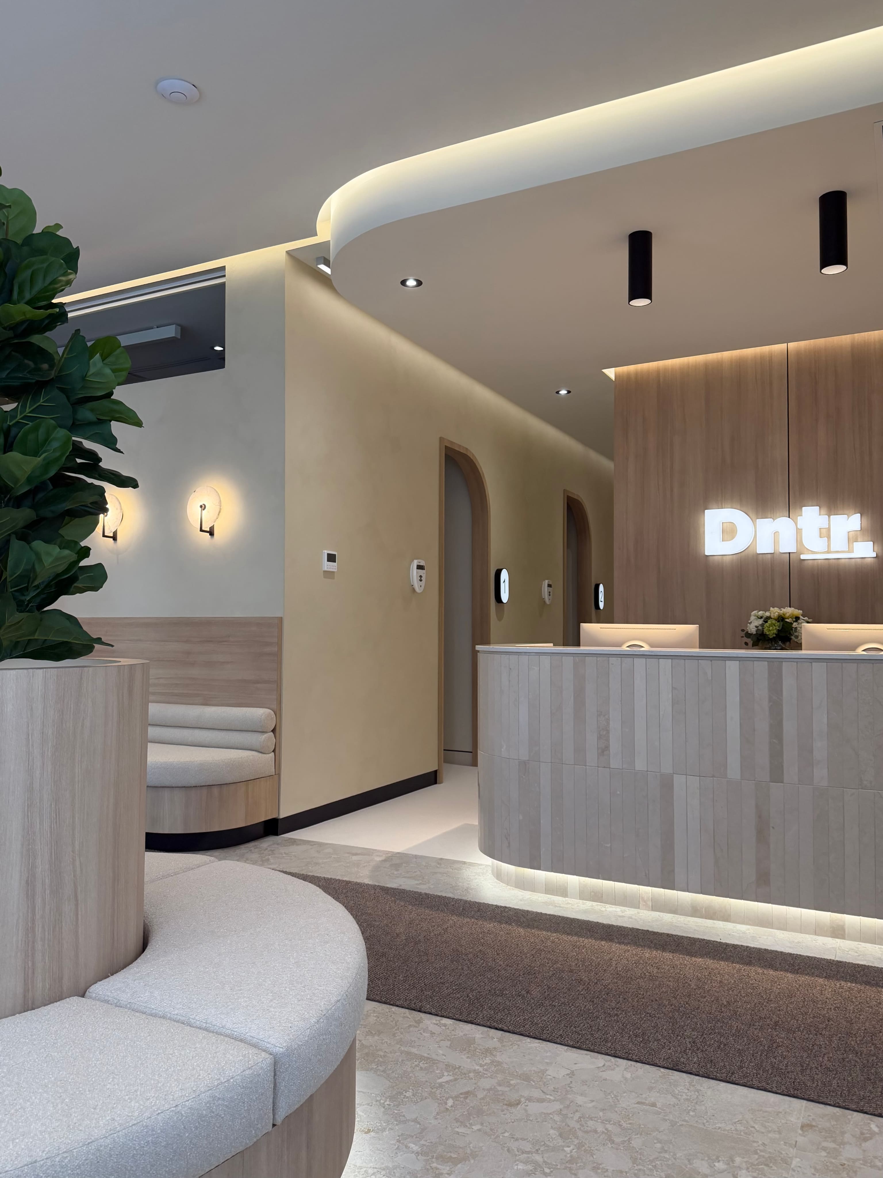 Intérieur moderne avec comptoir d'accueil, logo lumineux Dntr, deux cabines et une banquette.