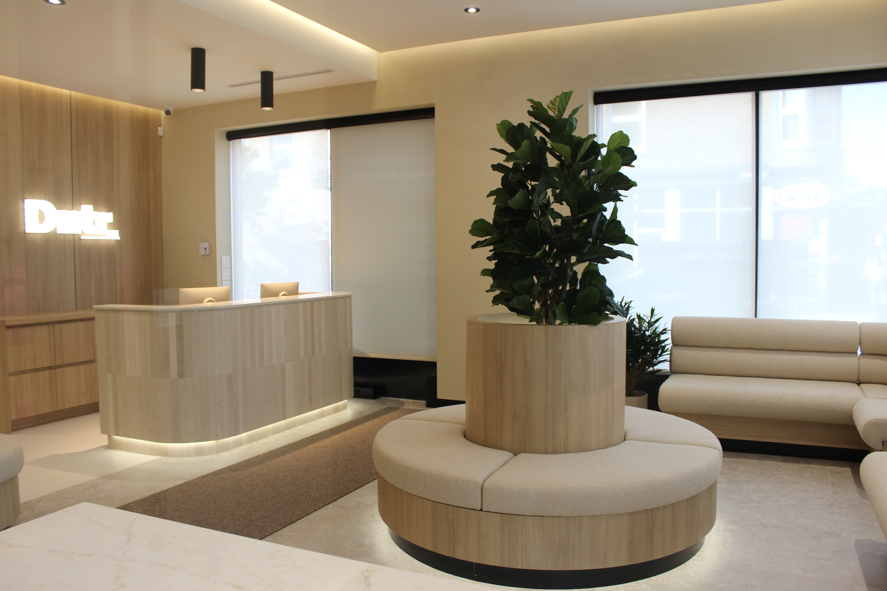 Intérieur d'une réception moderne avec comptoir, murs beige, signalétique et plantes vertes.