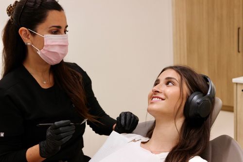Une patiente souriante avec casque et lunettes, examinée par une dentiste portant un masque noir.