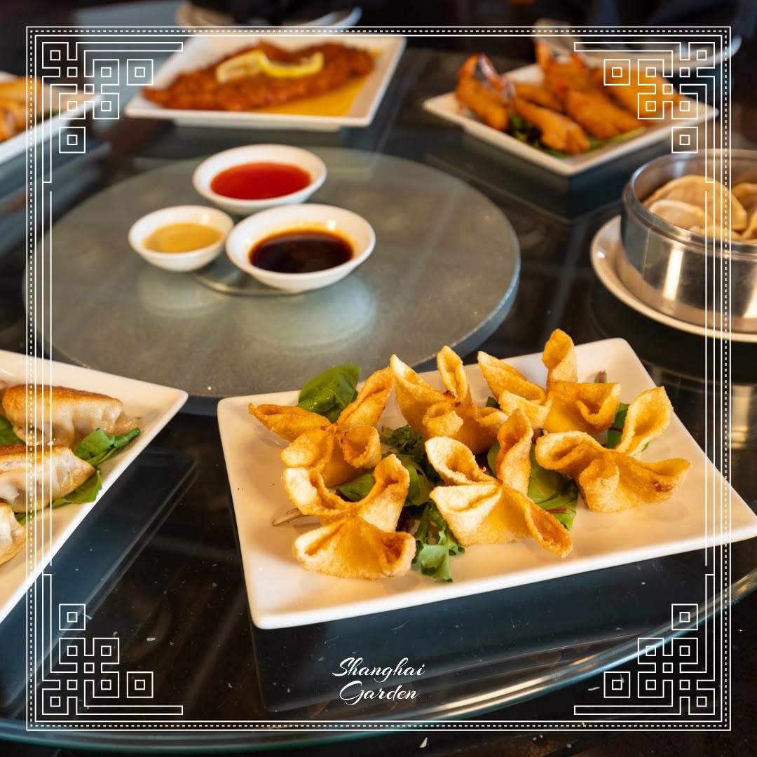 Various Chinese appetizers including fried wontons, dumplings, and dipping sauces on a glass table.