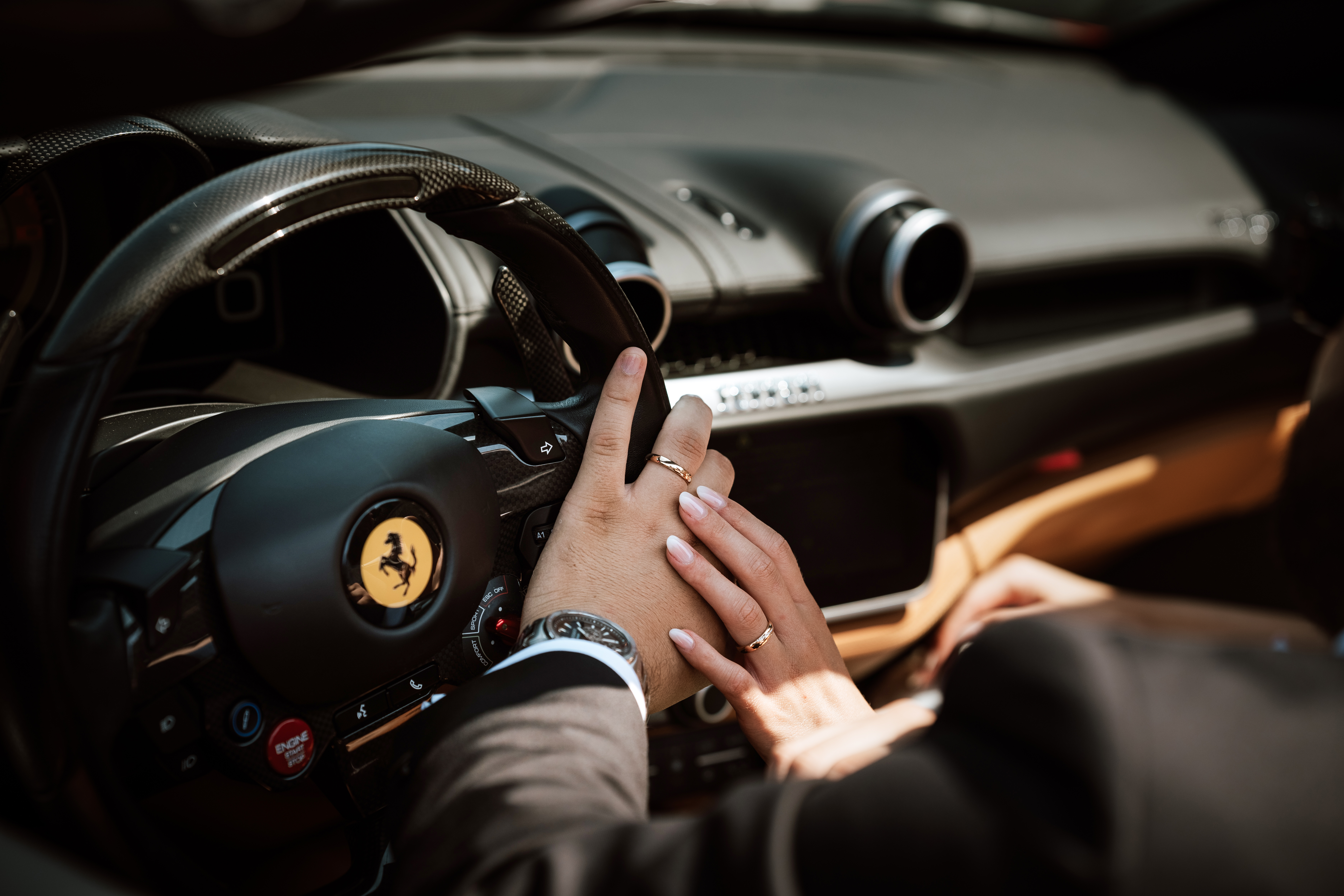 Le mani degli sposi con le fedi sul volante di una Ferrari