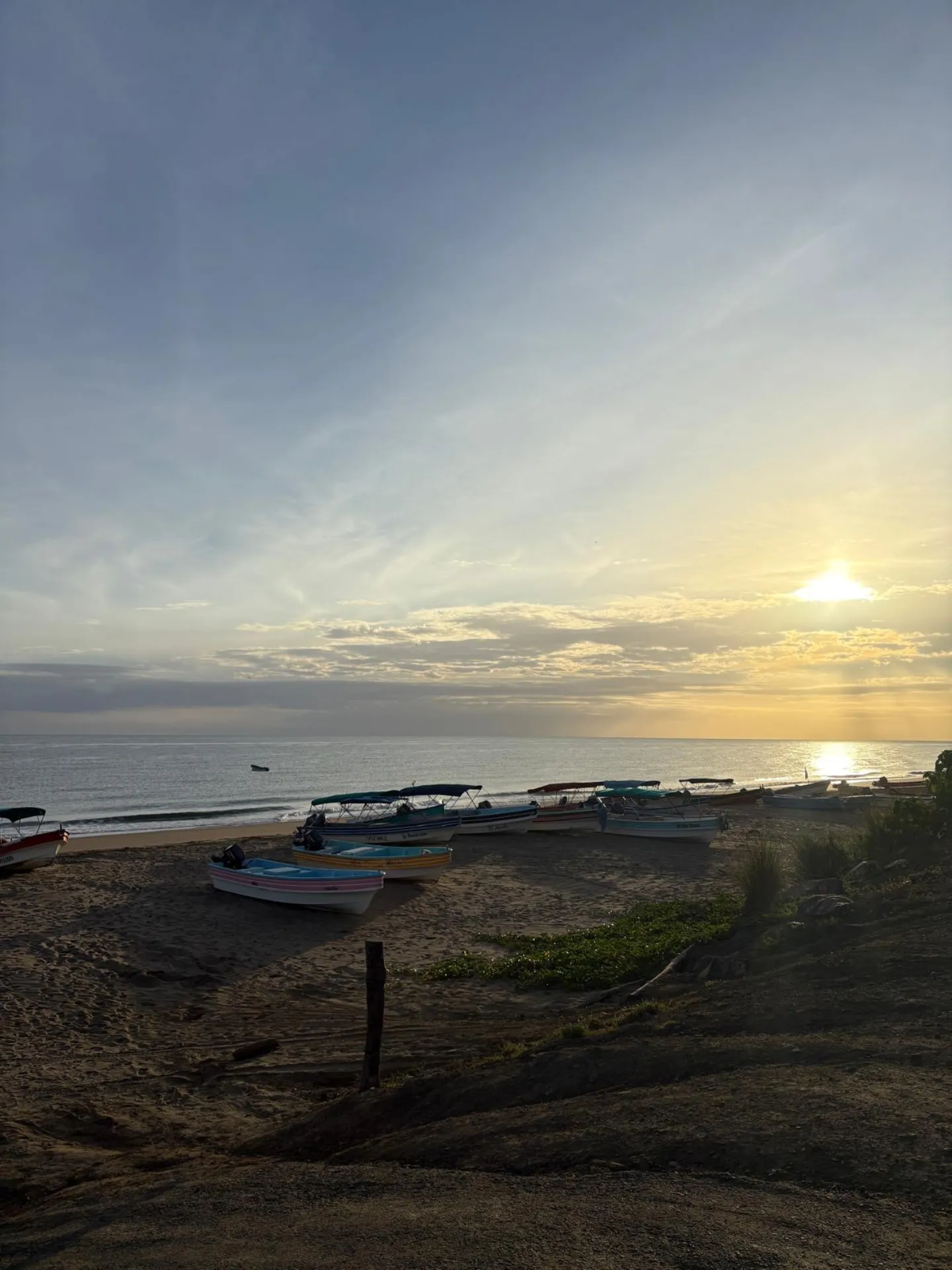 Plage au coucher du soleil avec plusieurs petits bateaux alignés sur le sable près des eaux calmes de l'océan.