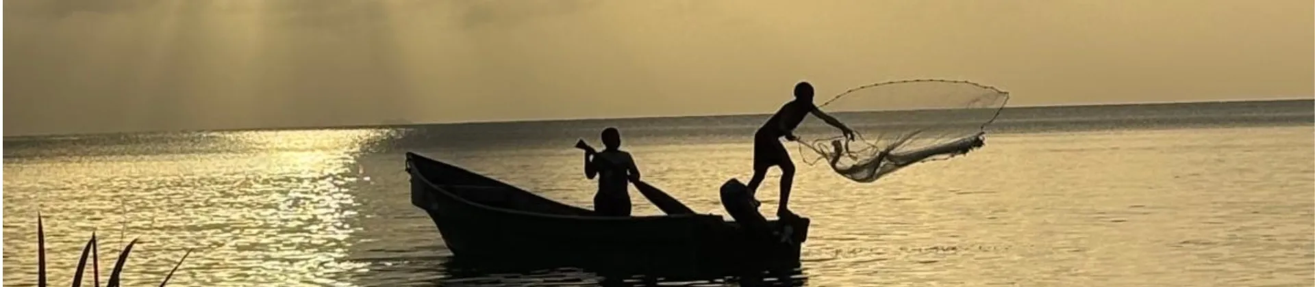 Deux personnes pêchant depuis un bateau au coucher du soleil, l'une jetant un filet sur une eau calme.