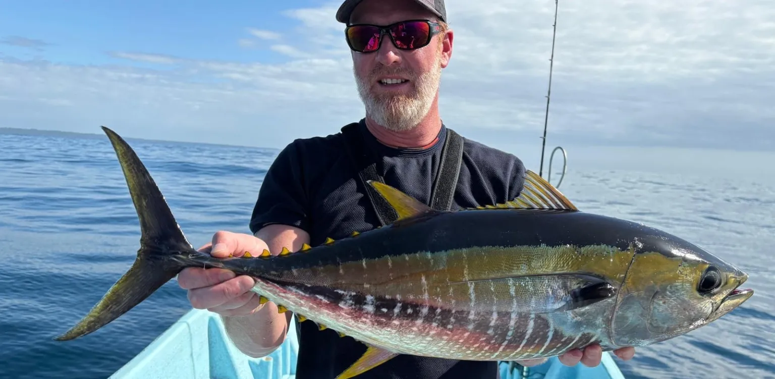 Homme tenant un grand thon albacore sur un bateau en pleine mer sous un ciel partiellement nuageux.