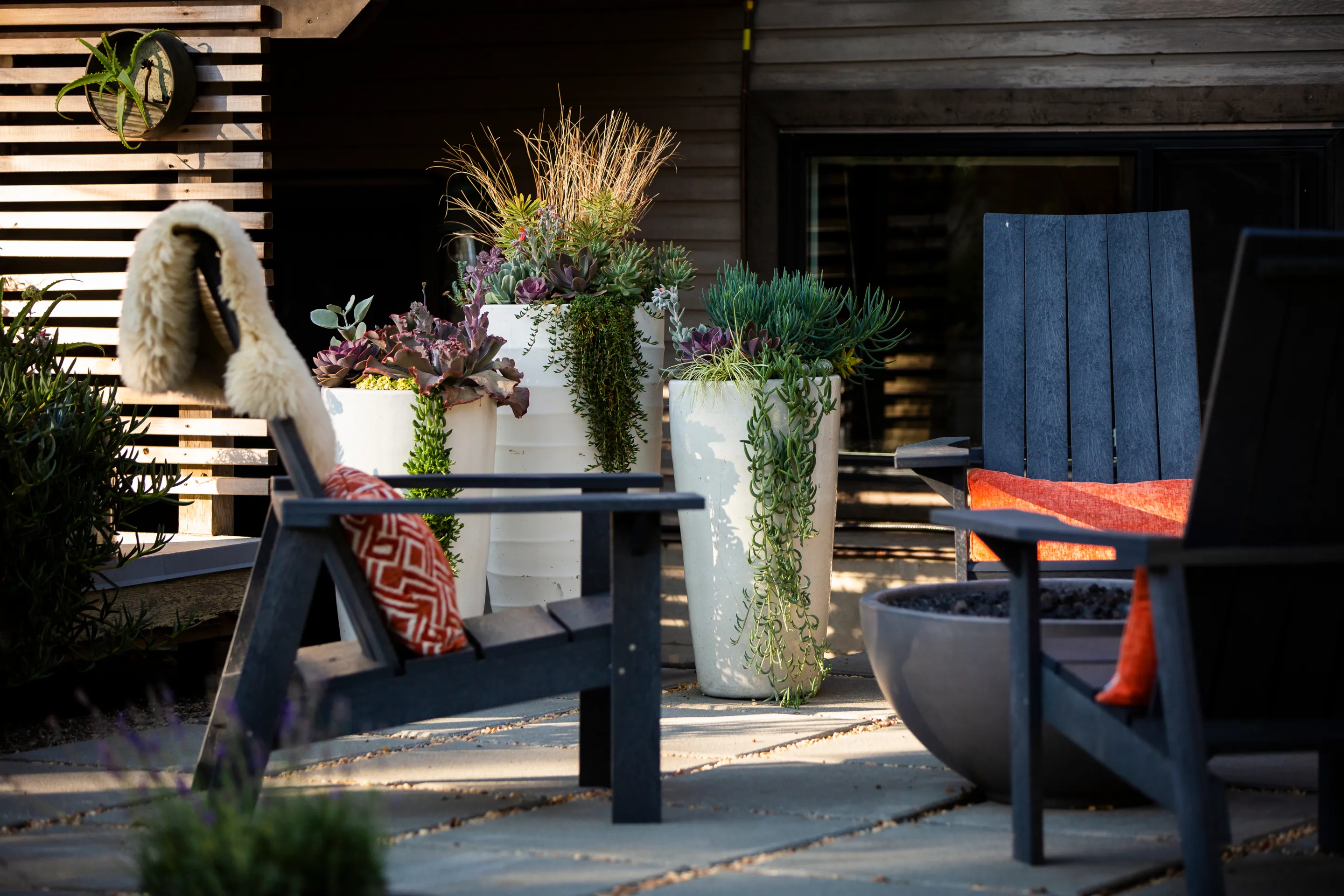 Sculptural planters on a dark-slatted patio with lounge chairs