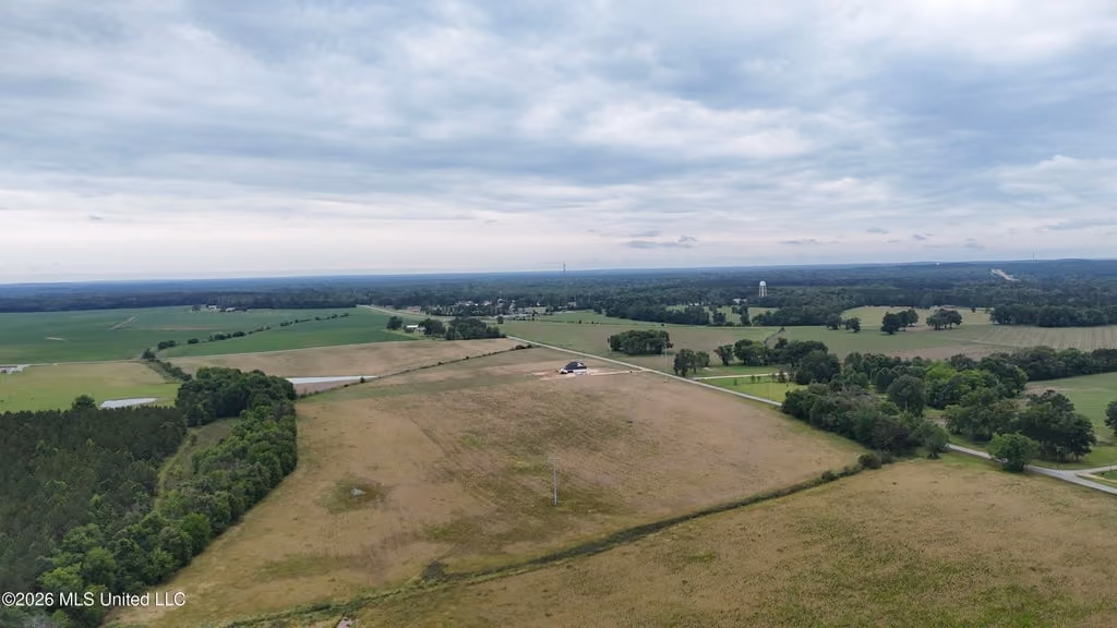 Aerial view of a Central Mississippi rural landscape with large open fields, scattered trees, a few small ponds, and a single building near the center under a cloudy sky.