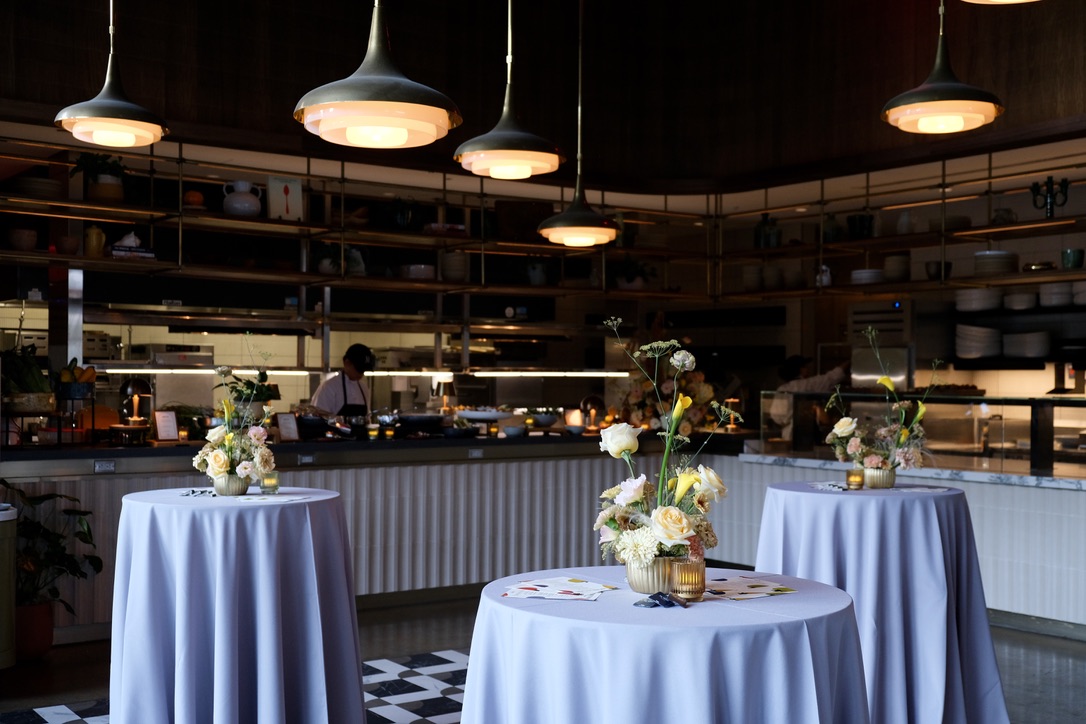 Cocktail tables dressed in linen with fresh florals in front of the open kitchen at The Morris Proper