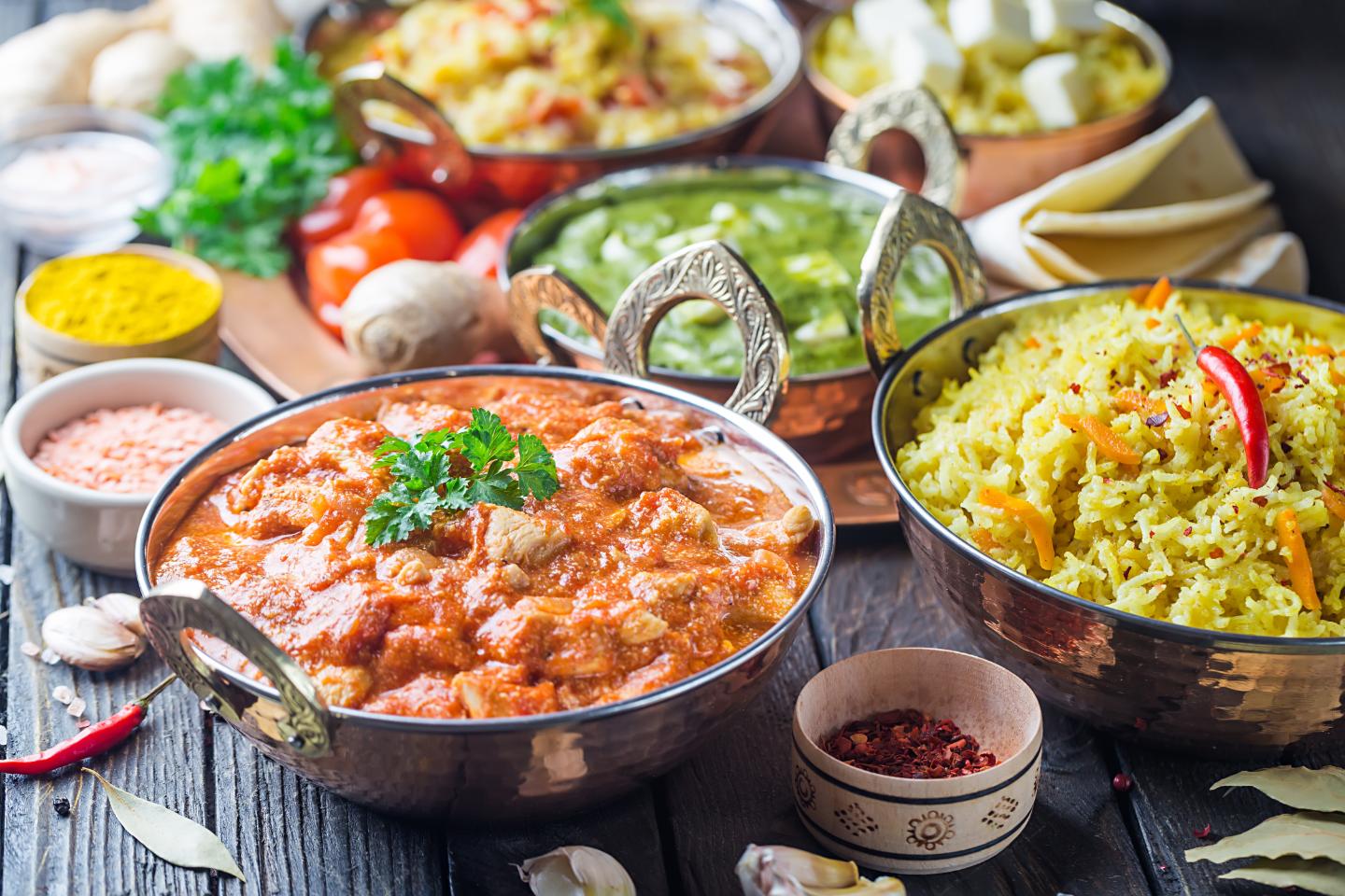 Indian curry, yellow rice with chili, green curry, and spices in traditional bowls on a wooden table.