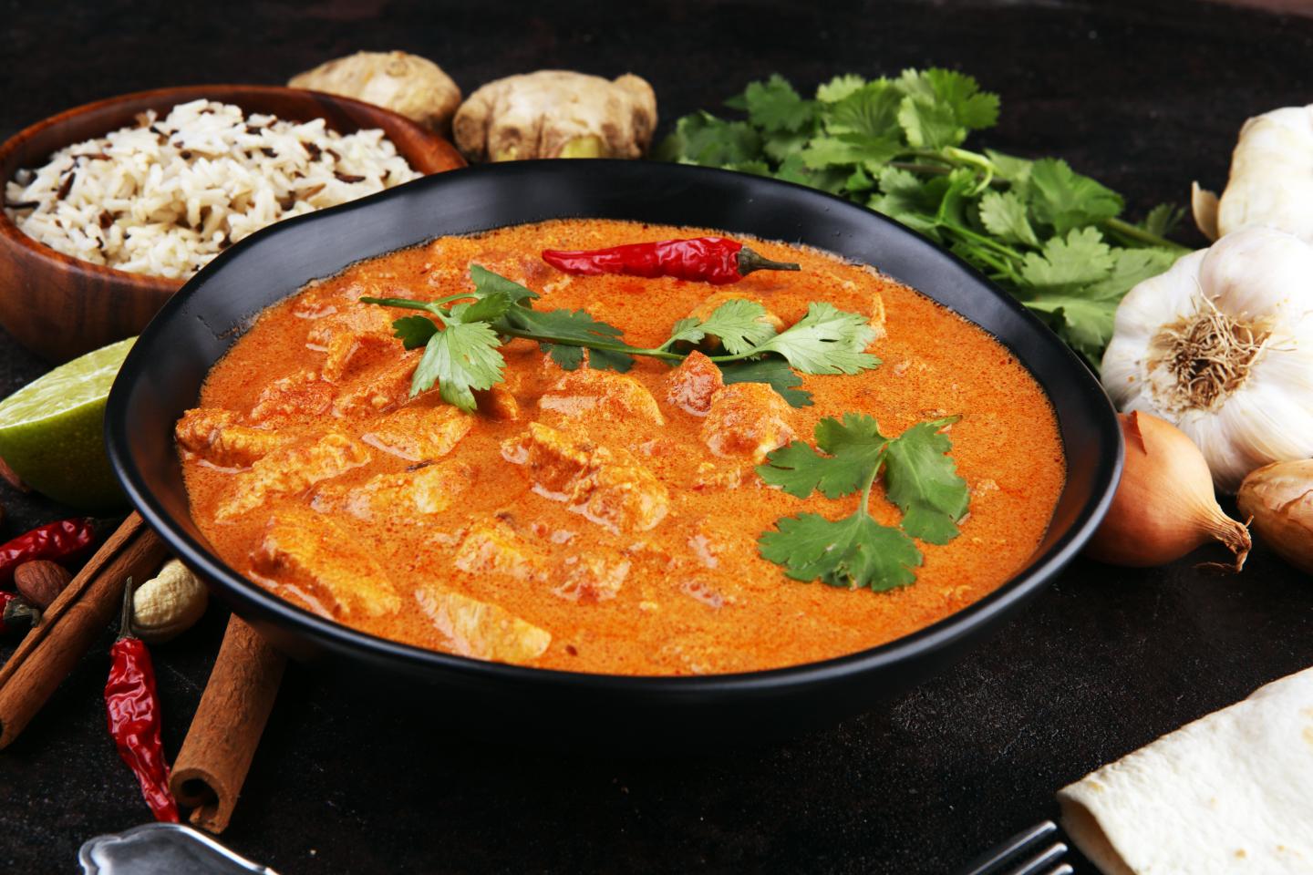 Bowl of creamy orange chicken curry garnished with cilantro and a red chili pepper.