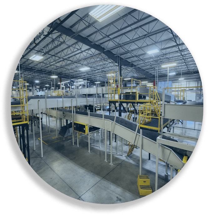 Interior view of a large industrial conveyor system in a warehouse with yellow railings and high ceilings.