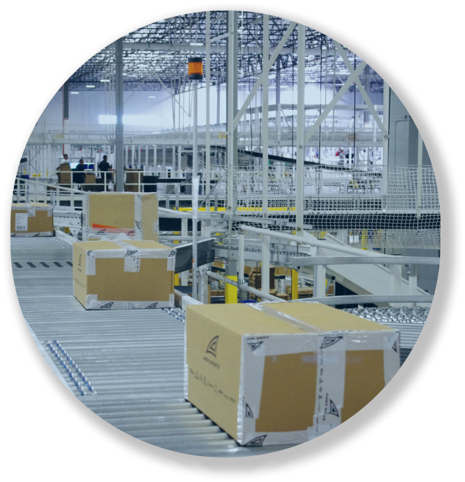 Cardboard boxes move along a conveyor belt system in a large warehouse or distribution center.
